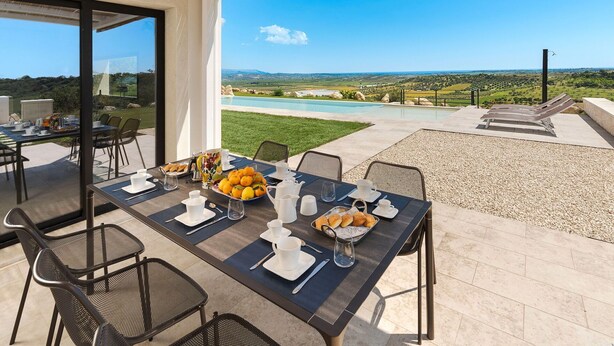 Comedor con una mesa dispuesta para el desayuno, con vistas a una piscina y un paisaje pintoresco.