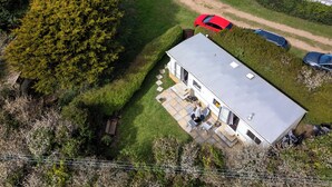 Une vue aérienne d’une maison de plain-pied dotée d’un patio, d’une voiture rouge garée dans l’allée et d’un grand arbre situé à gauche.