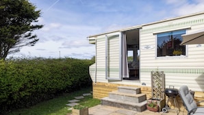 Une maison mobile dotée d’une porte coulissante, d’un petit porche, d’un barbecue et d’une chaise.
