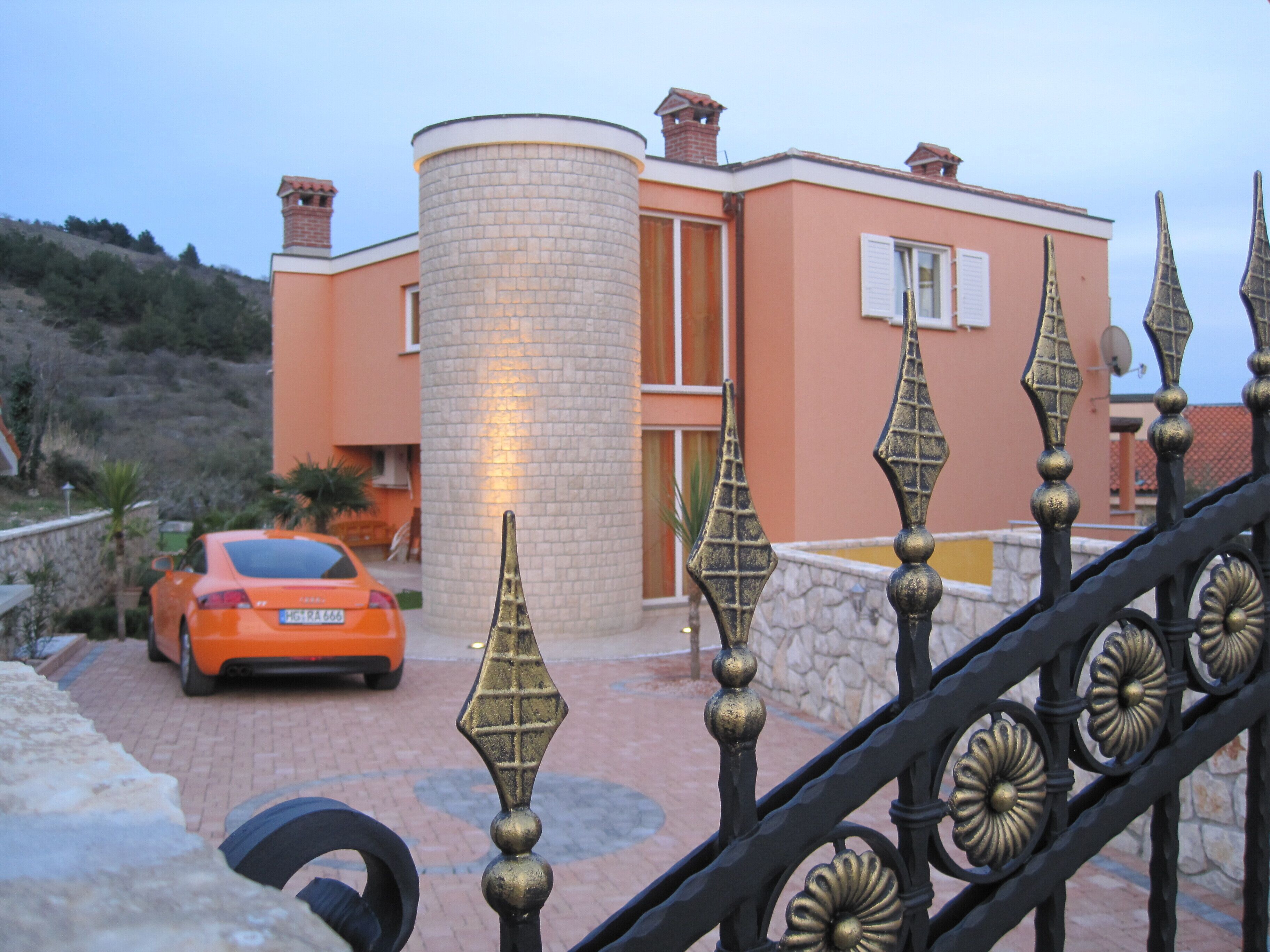 A modern building with a cylindrical tower, a car parked in front, and a decorative metal fence.