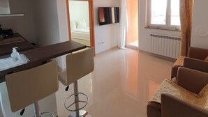 A spacious living area with a sofa, a dining table with chairs, a TV mounted on the wall, and a large window with curtains. - 4-Star Comfort Apartment with Ocean View, Rabac, Croatia (Rabac)