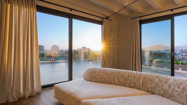Una sala de estar moderna con un sofá grande, ventanas amplias y vistas a un paisaje urbano.