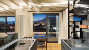 Una cocina moderna con una isla integrada, un comedor con mesa de vidrio y vistas a la ciudad y montañas a través de grandes ventanales.