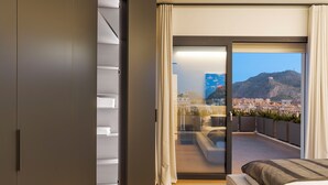Un dormitorio moderno con una cama grande, un ventanal corredero a un balcón y vistas a la ciudad.