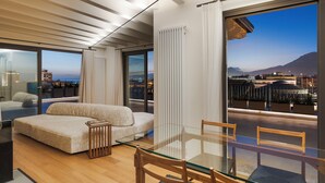 Una sala de estar moderna con una mesa de comedor de vidrio, sillas de madera, un sofá y vistas a la ciudad a través de amplias ventanas.