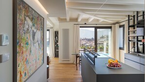 Cocina moderna con una isla grande, comedor con mesa de vidrio y vista a un paisaje urbano a través de amplios ventanales.