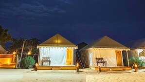 Uma fileira de tendas com um palco e área de assentos, ao fundo um céu noturno com a lua visível.