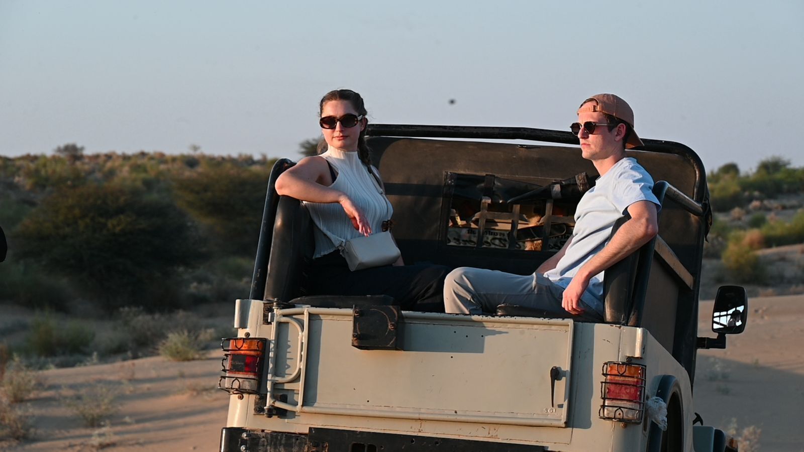 Two people in a vehicle with a rear cargo area, a side mirror, and a license plate.