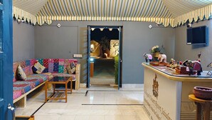Ampla sala de estar com pé direito alto, sofá estampado, mesa de centro de madeira e balcão de recepção com uma placa.