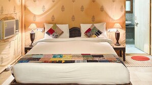 Quarto tipo tenda com cama, duas luminárias de mesa, dossel estampado e vista para um banheiro.