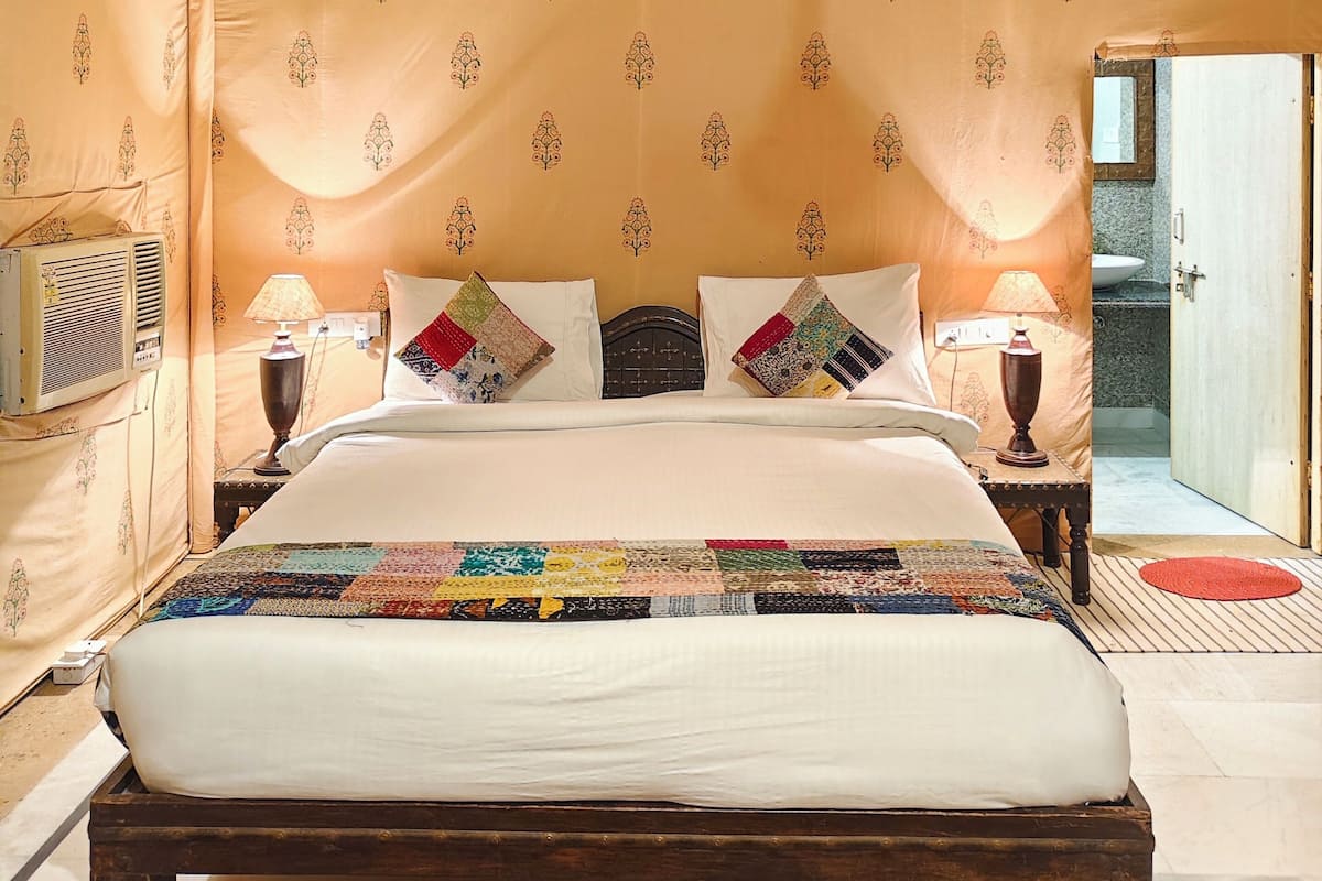 A tent-style room with a bed, two bedside lamps, a patterned canopy, and a view of a bathroom.