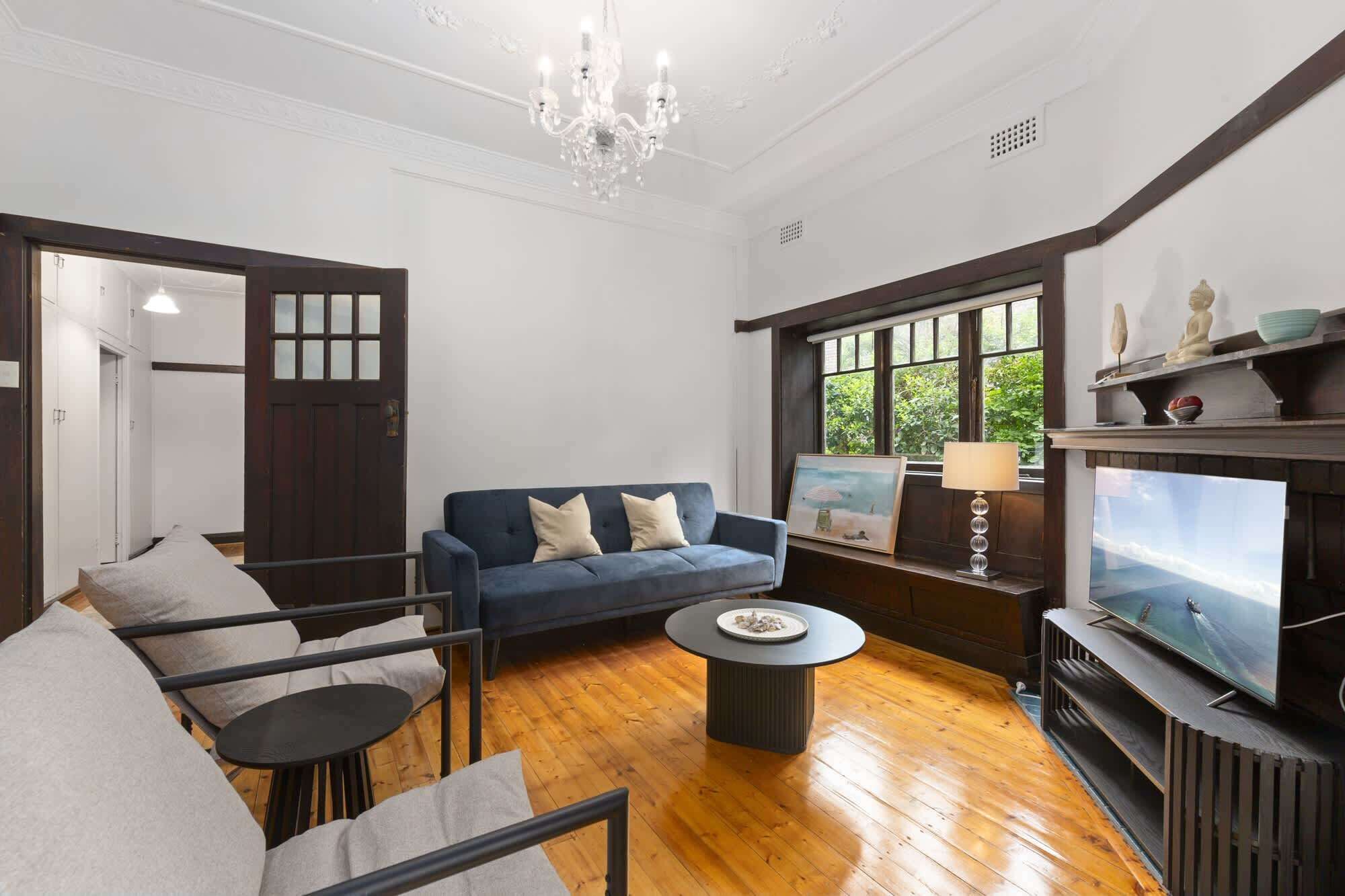 A living room with a dark blue sofa, a round coffee table, a TV on a wooden stand, and a chandelier.