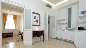 Eine moderne Küche mit weißen Schränken, einer Mikrowelle und einem Spülbecken. Es gibt einen Essbereich mit Tisch und Stühlen, sowie ein Fenster mit Vorhängen.