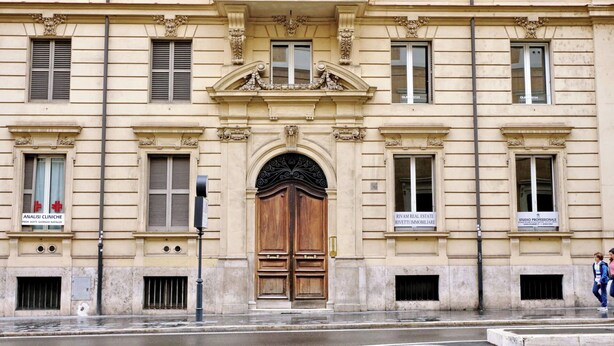 Ein historisches Gebäude mit einem zentralen Eingang, zahlreichen Fenstern und Schilder für Geschäfte.