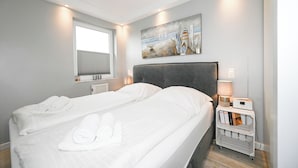 Ein Hotelzimmer mit zwei Betten, einem Kopfteil, einem Nachttisch mit Lampe, einem Wandbild und einem Fenster mit Jalousien.