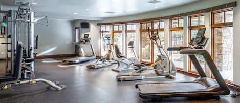 A gym with various exercise equipment, large windows, and a speckled floor.