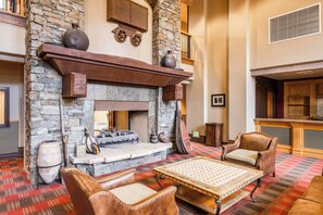 A stone fireplace with a mantel, a log fire, and a seating area with leather chairs and a woven table. - 2BR Canyons Ski-in/Ski-out With Resort Amenities (Park City)