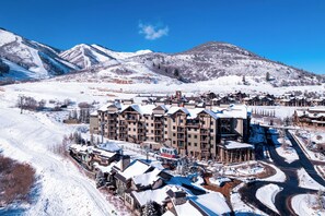 A snow-covered resort with multiple buildings, including a large hotel with a ski lift visible in the background. - 2BR Canyons Ski-in/Ski-out With Resort Amenities (Park City)