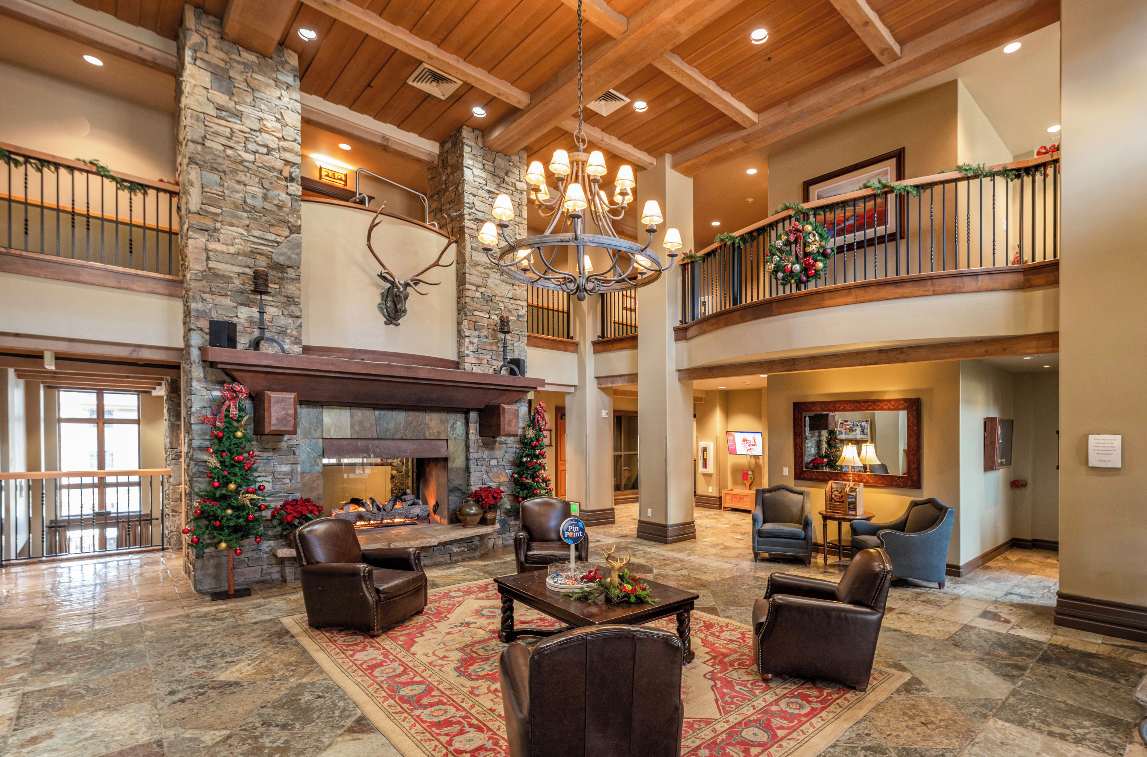 A spacious lobby with a stone fireplace, leather seating, a chandelier, and a Christmas tree.