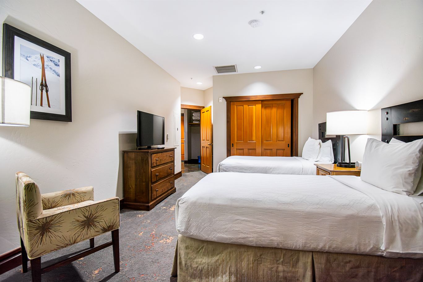 A hotel room with a bed, a television on a dresser, a chair, and a wooden door.