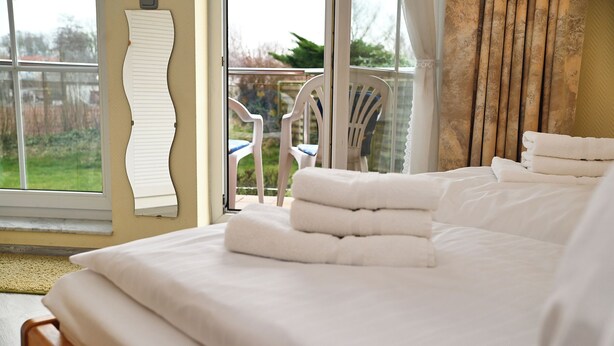 A hotel room with a bed, a chair, and a view of the outdoors. - Küstenwind: Cozy 2-room apartment with use of swimming pool (Büsum)