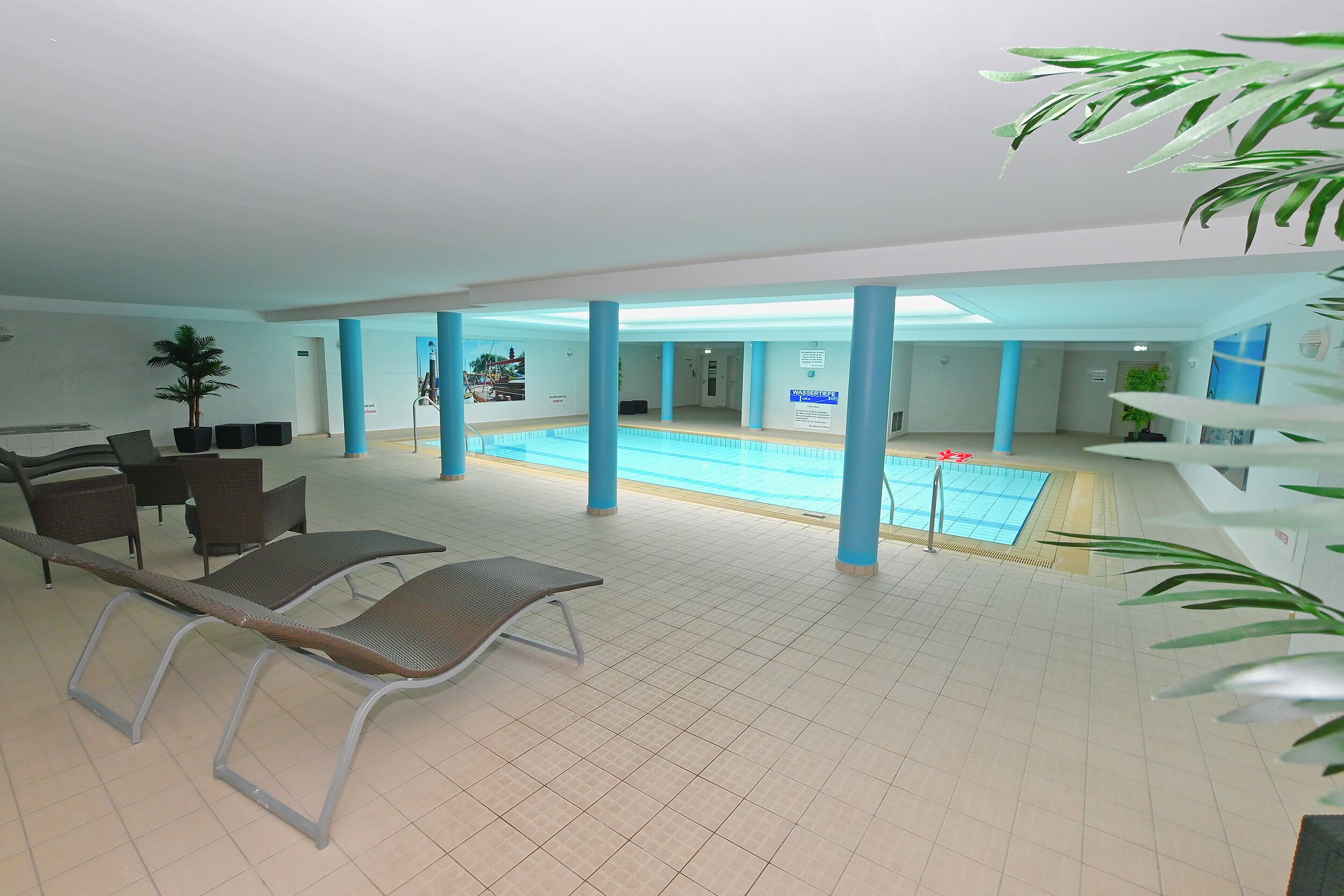 A spacious indoor swimming pool area with lounge chairs and a tiled floor.