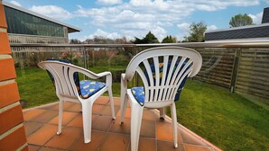 A patio with two white plastic chairs and a table. - Küstenwind: Cozy 2-room apartment with use of swimming pool (Büsum)
