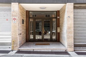 Una entrada de edificio con puerta de vidrio, portón metálico y felpudo.