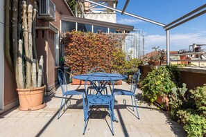 Un patio con mesa y sillas, rodeado de plantas en macetas y un cactus grande.