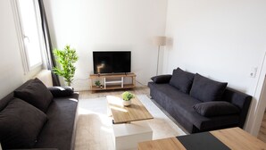 A modern living room with a dark sofa, a wooden coffee table, and a flat-screen TV on a stand. - ME LIVING 1: Hauptallee - Bad Pyrmont - Apartment (Bad Pyrmont)