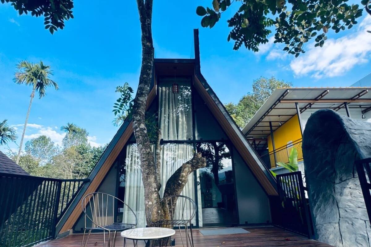 Un edificio moderno dalla forma triangolare, con una terrazza in legno, un tavolo e delle sedie.