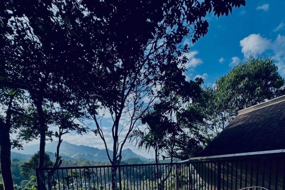 Un terrazzo in legno all'aperto con un tavolo rotondo e sedie in metallo, circondato da una ringhiera metallica, affacciato su un paesaggio montuoso.