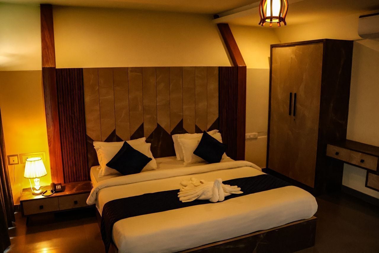A hotel room with a large bed, a nightstand with a lamp, a wardrobe, and a wooden headboard.