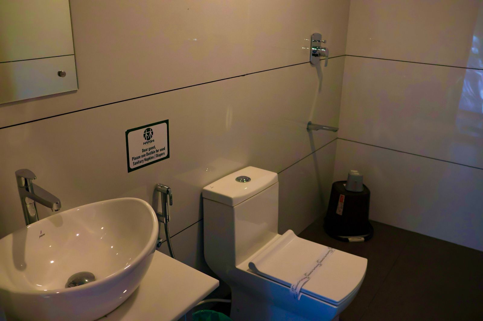 A bathroom with a sink, toilet, and shower. A sign instructs to use disposable sanitary napkins or diapers.