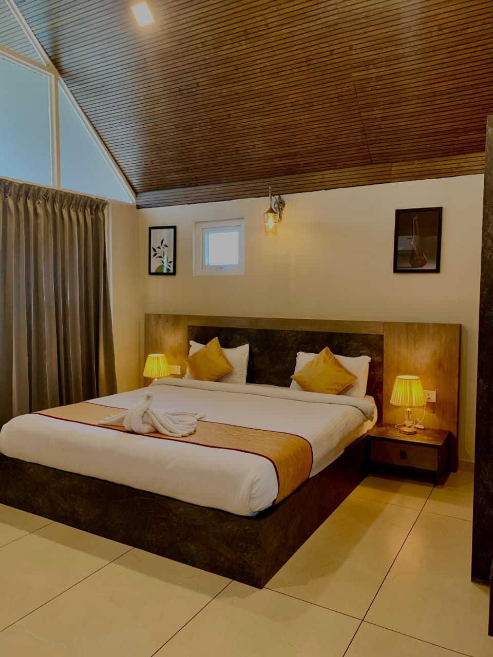 A hotel room with a large bed, two bedside lamps, a window, and a ceiling with wooden slats.