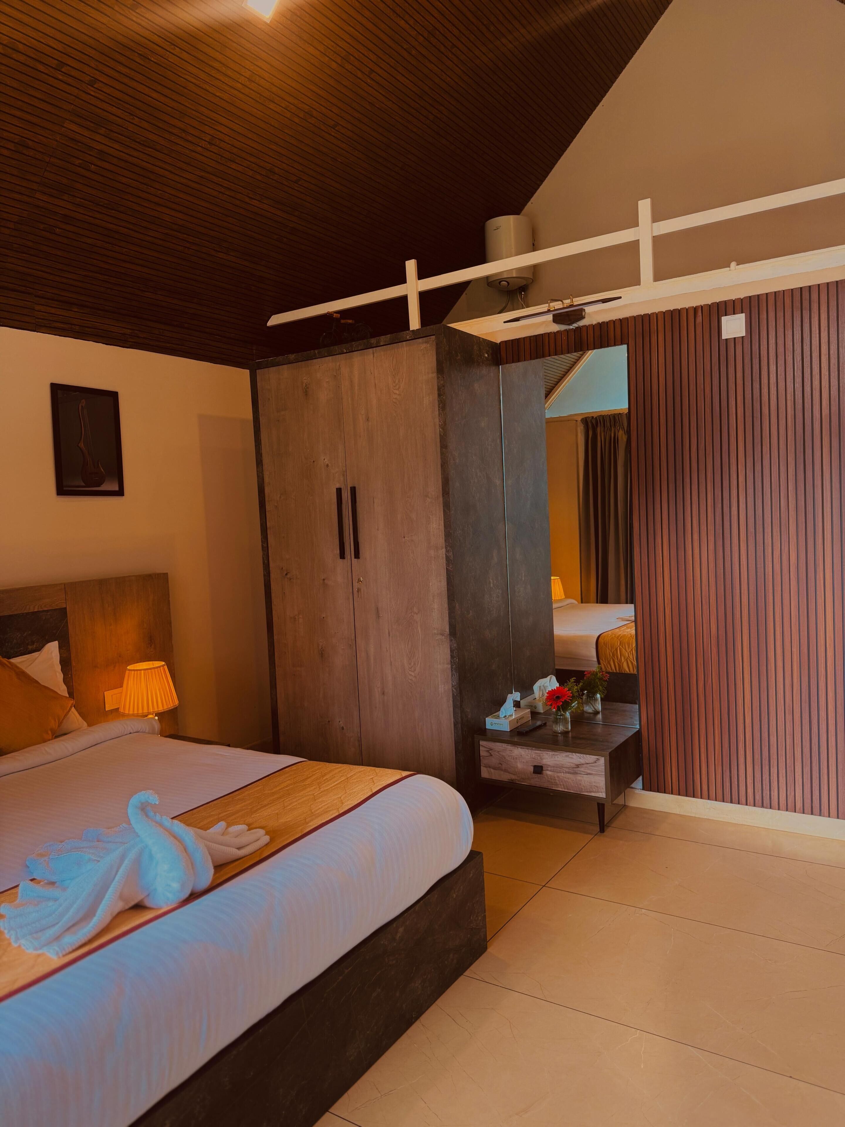 Une chambre d’hôtel avec un lit, une armoire en bois, une table de chevet avec une lampe et un miroir qui reflète la pièce.