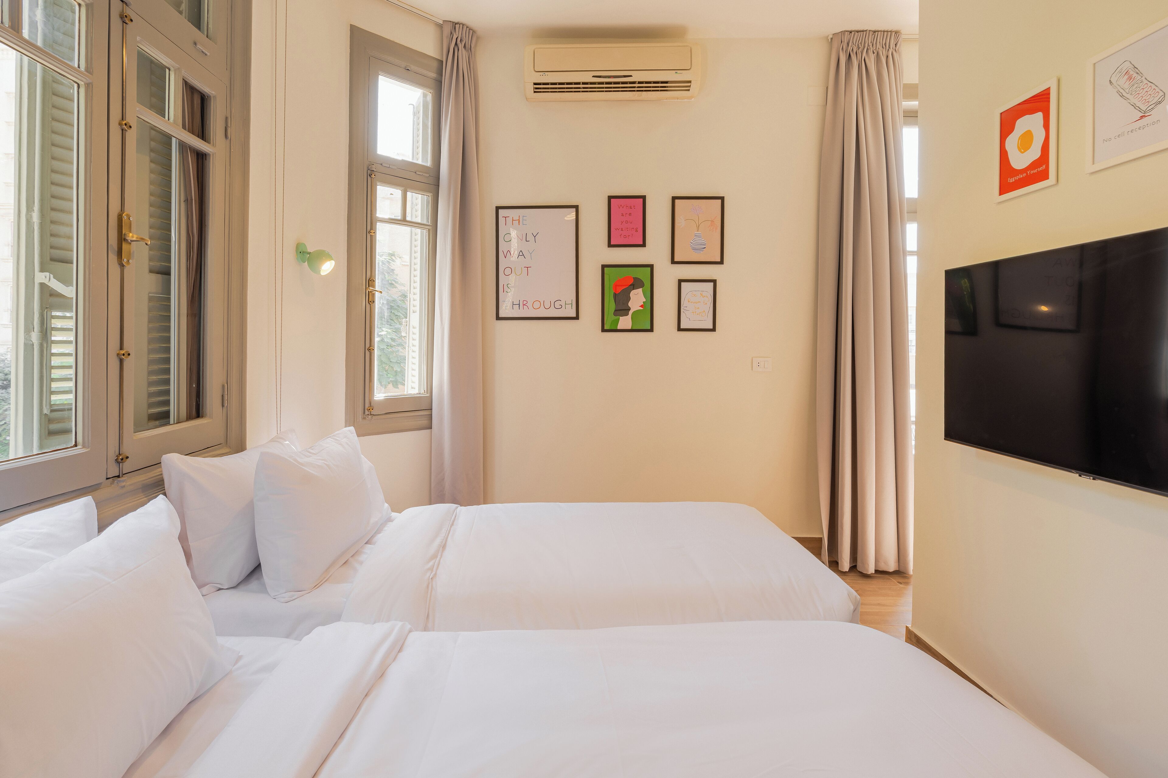 Une chambre d’hôtel avec deux lits, une télévision et des œuvres d’art accrochées aux murs.