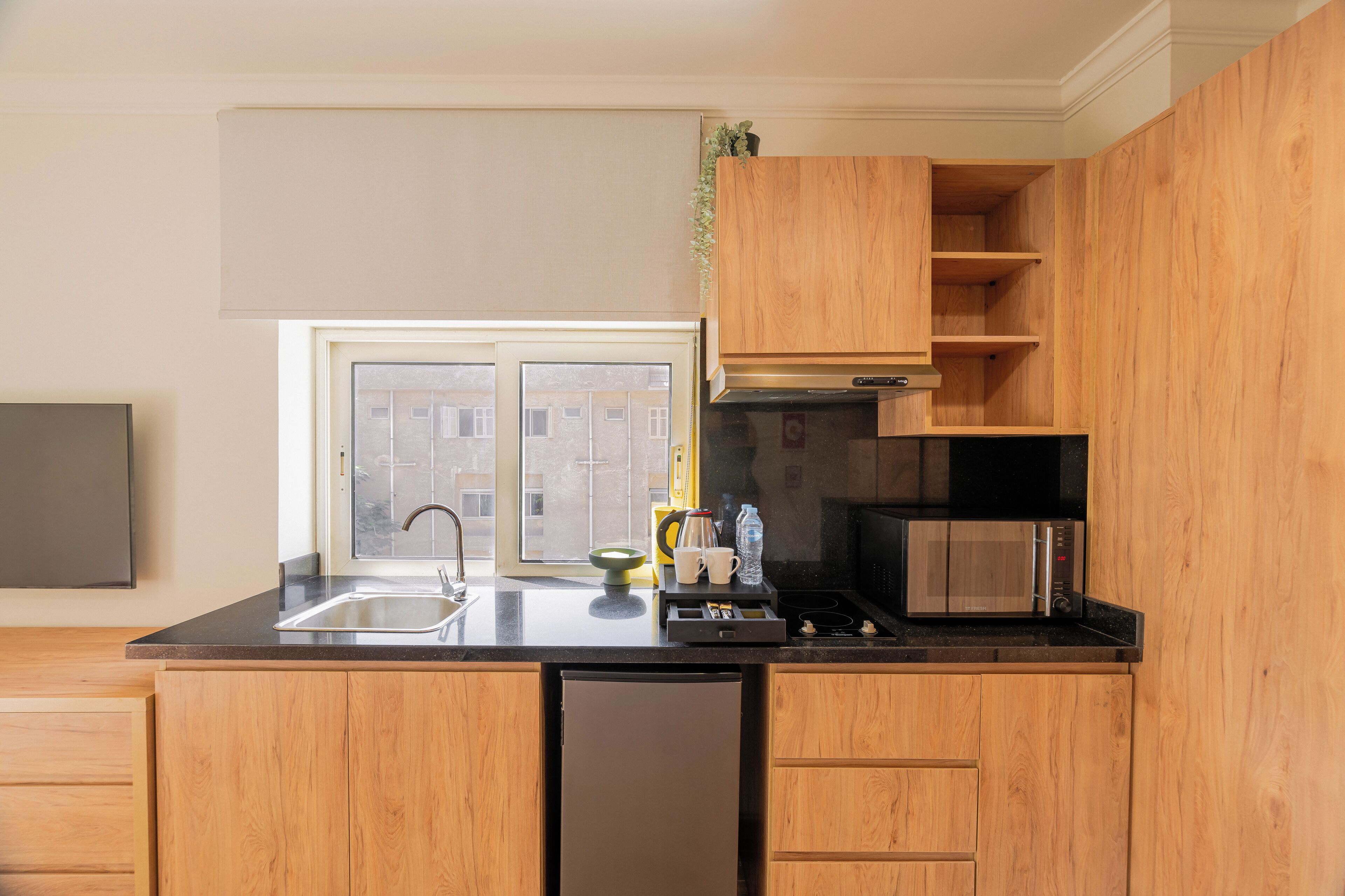 Una cocina moderna con armarios de madera, encimera negra, microondas empotrado y ventana con vistas a edificios.