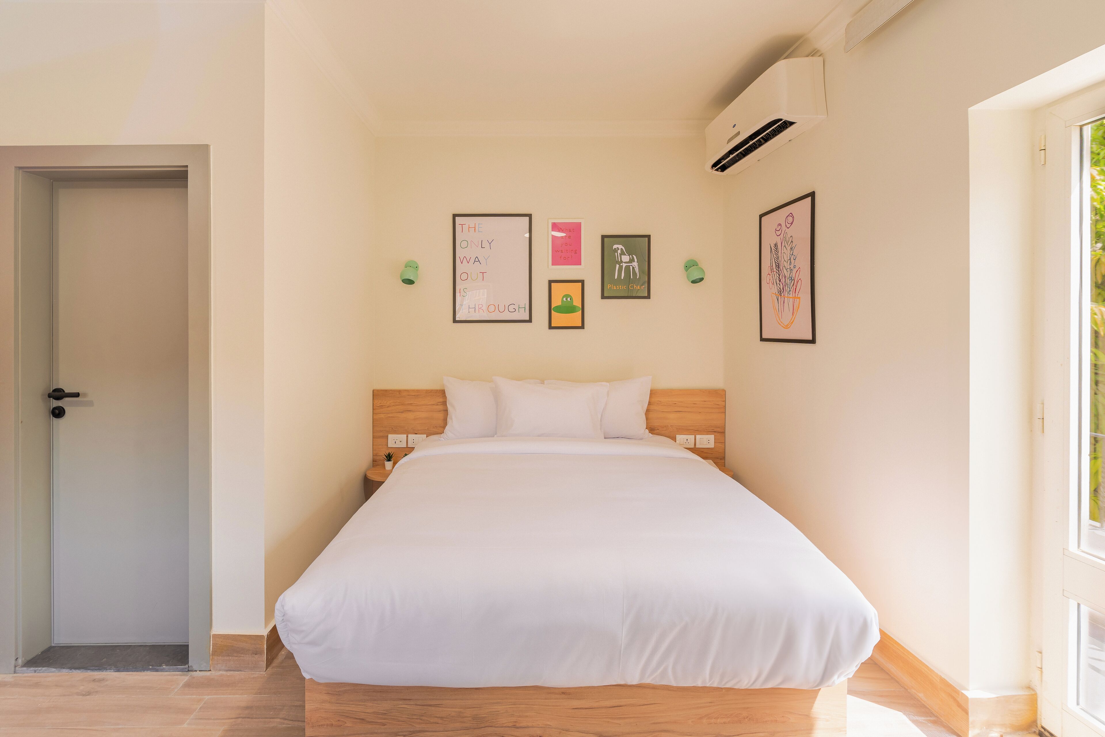 Un dormitorio con una cama grande, una puerta, aire acondicionado instalado en la pared y cuadros enmarcados.
