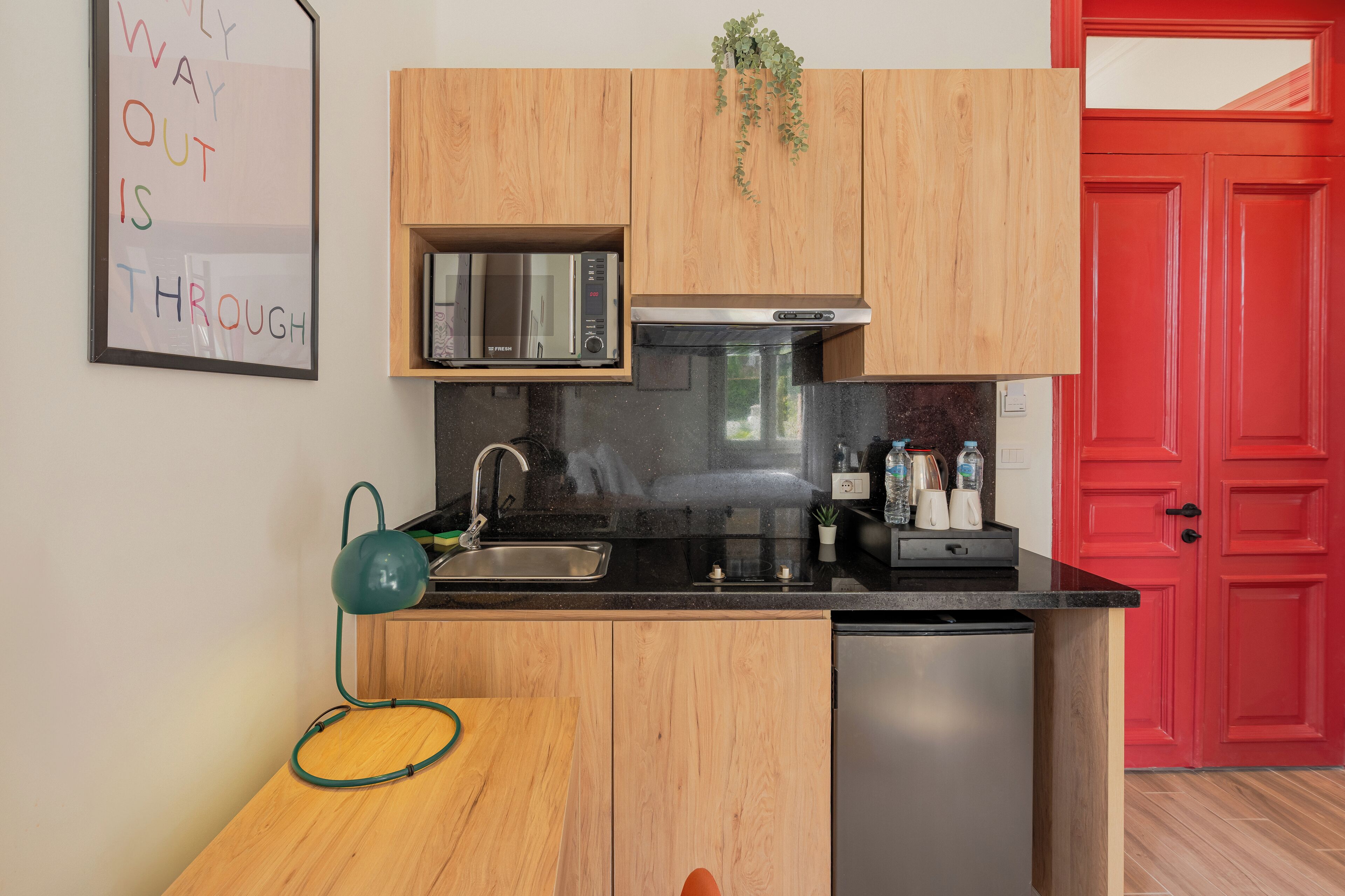 Cozinha compacta com armários de madeira, pia de aço inoxidável e uma porta vermelha.