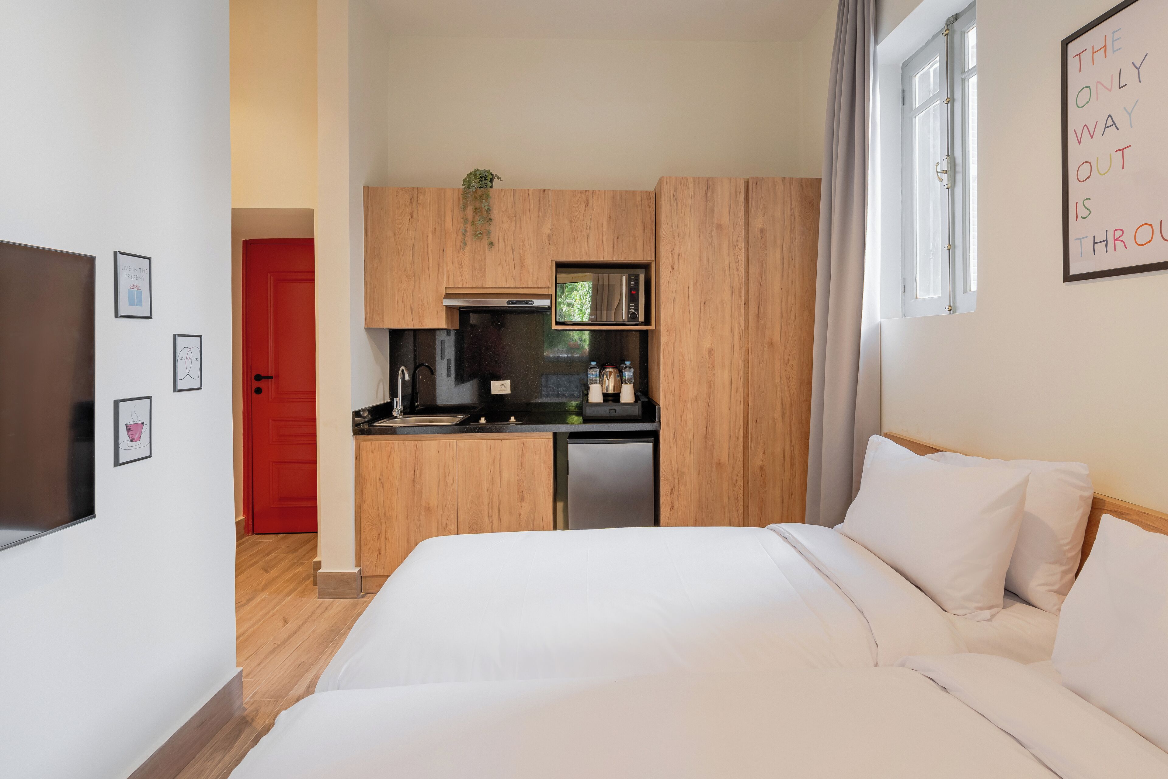 Una habitación de hotel moderna con una kitchenette de madera, una cama con ropa blanca y una puerta roja.