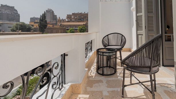 A balcony with two chairs and a small table, overlooking a cityscape with buildings and trees. - Brassbell Zamalek Daoud Studios Villa A (Cairo)