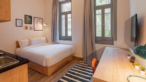 A bedroom with a bed, a desk, a TV, and a window with curtains. - Brassbell Zamalek Daoud Studios Villa A (Cairo)