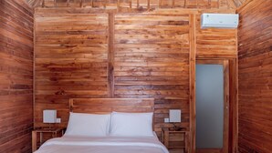Ein Zimmer mit Holzwänden, einem Bett, zwei Nachttischen und einer Klimaanlage.