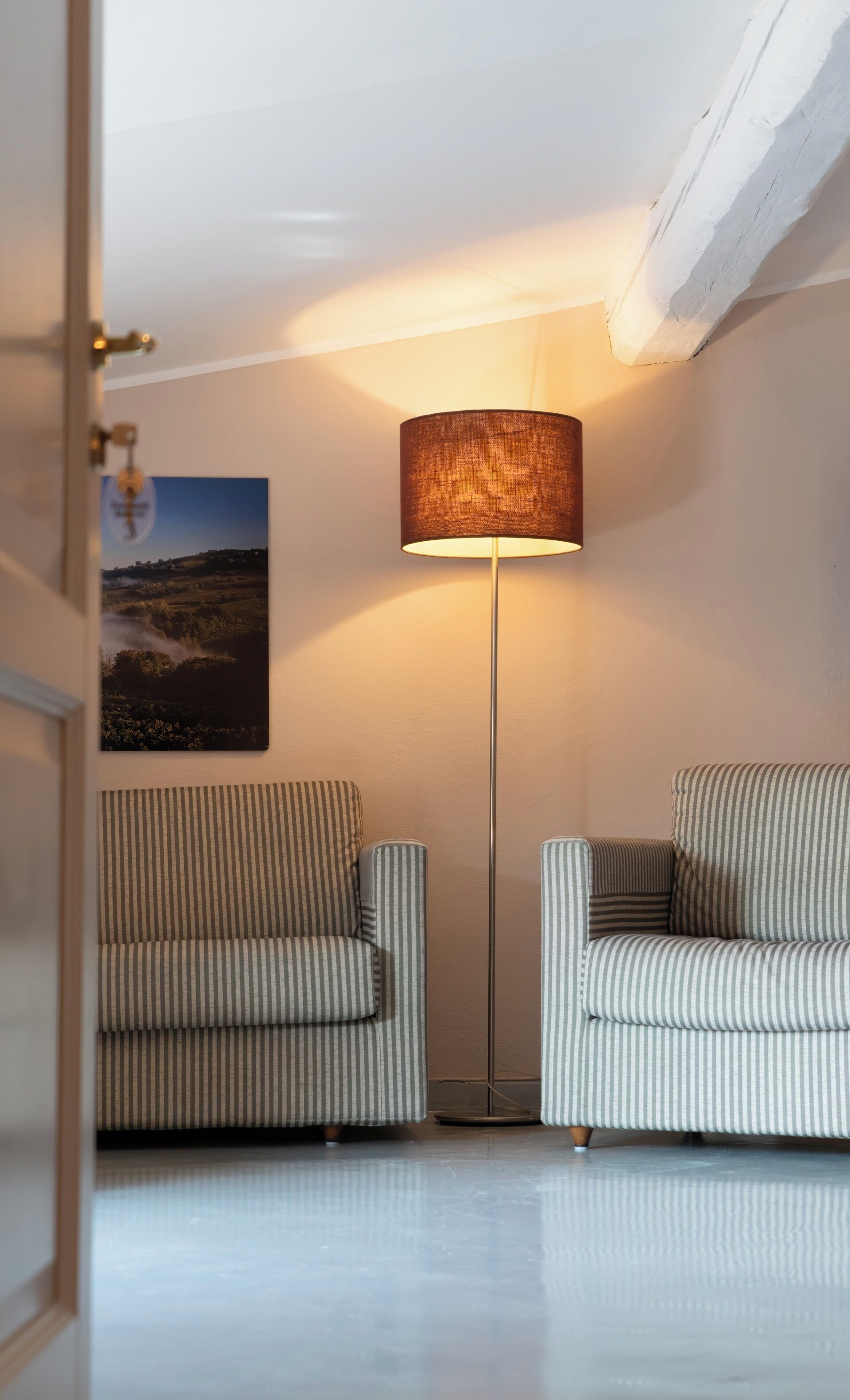 Una habitación con dos sillones a rayas, una lámpara de pie y un cuadro con un paisaje en la pared.