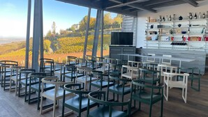 Un restaurant doté d’une terrasse donnant sur un vignoble, avec des tables et des chaises en bois, un téléviseur et un présentoir à vins.