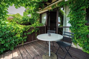 A wooden deck with a round table and two chairs, surrounded by lush green foliage. - Foresteria Settevie (Treiso)