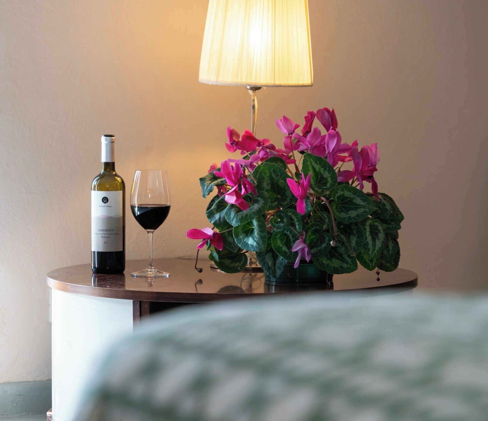 En vinflaske, et vinglas og en potteplante med lyserøde blomster på et rundt bord.