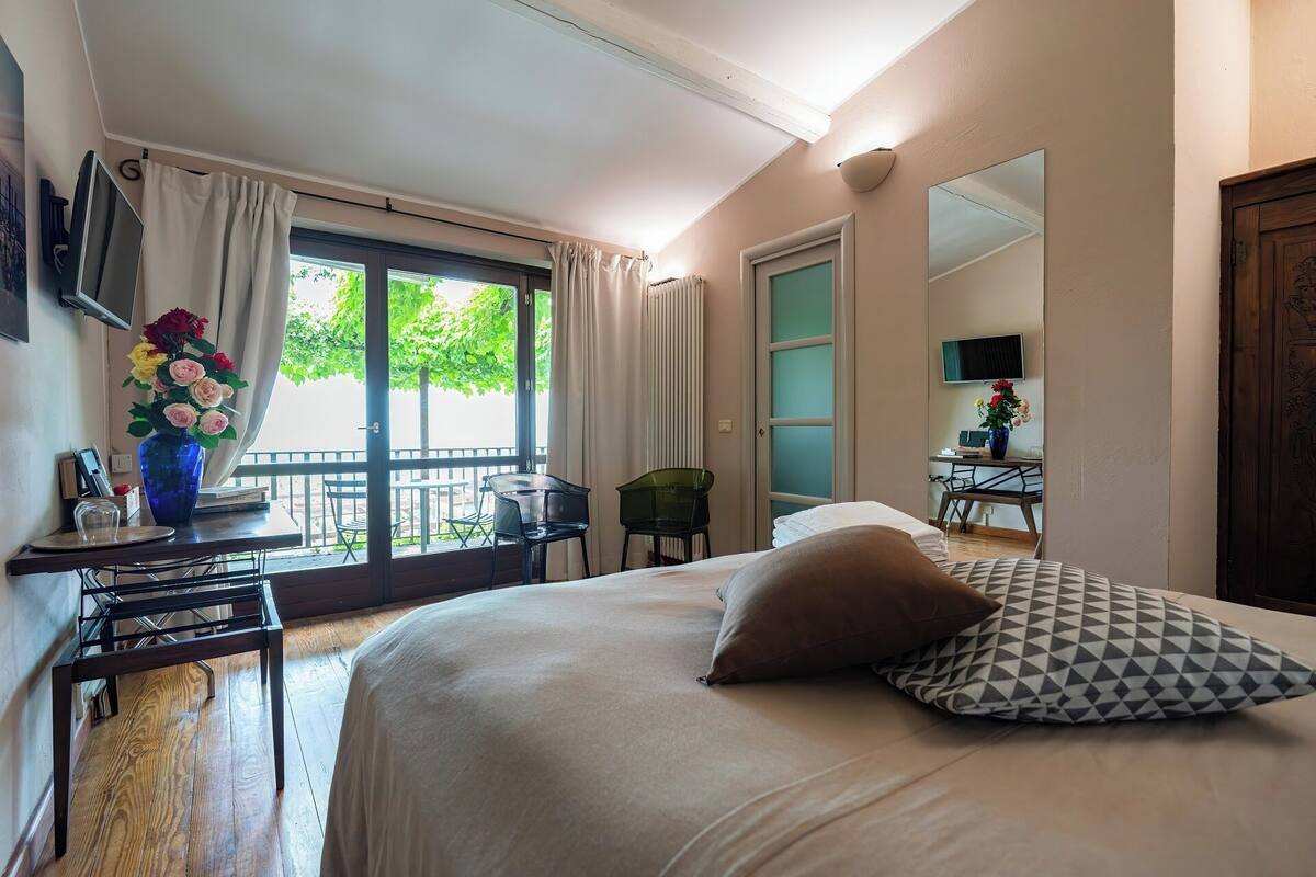 Une chambre d’hôtel avec un lit, un bureau, une chaise et une grande fenêtre avec des rideaux.