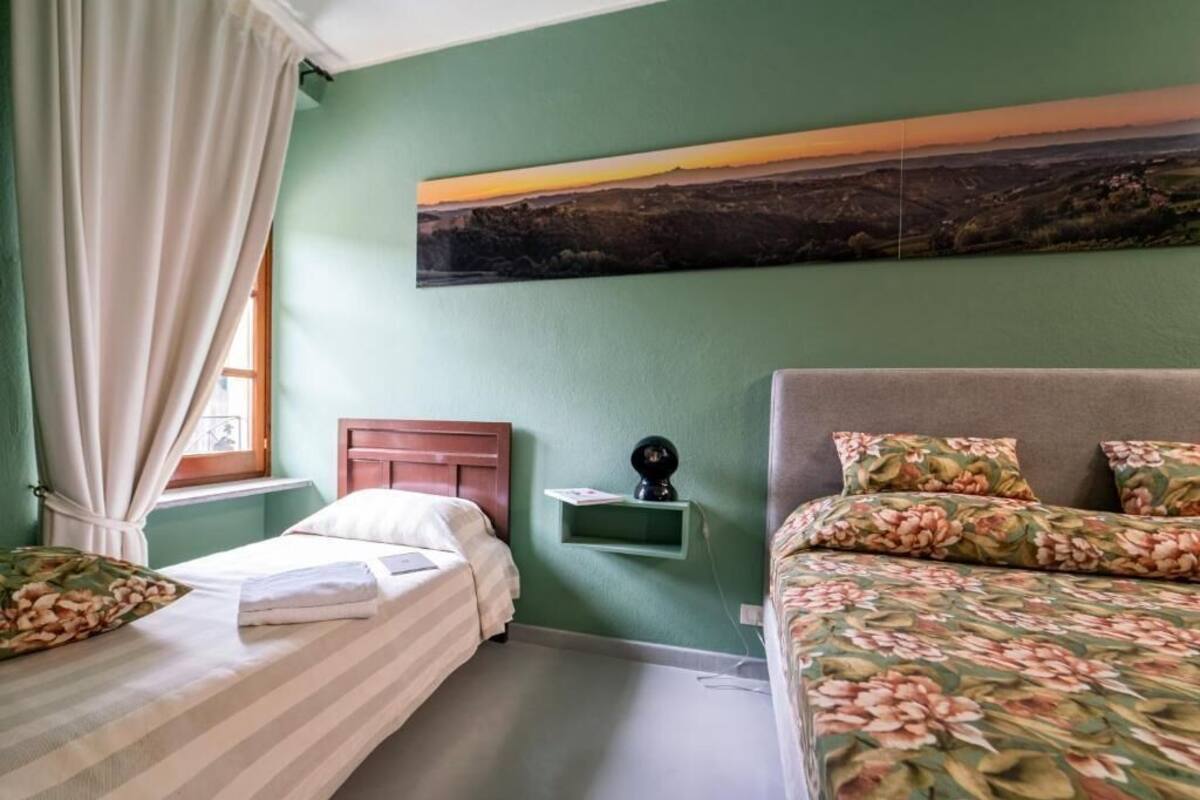 Une chambre avec deux lits, un mur vert, un tableau et une table de chevet avec une lampe.